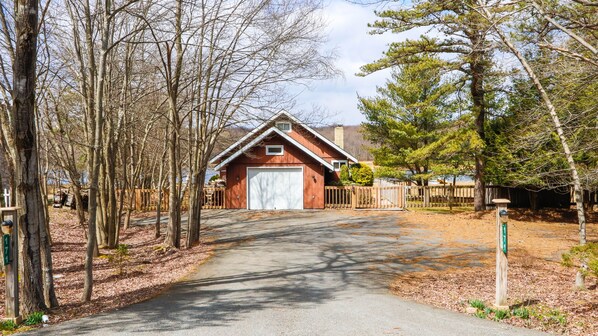 A red garage with a white door, surrounded by trees and a wooden fence.