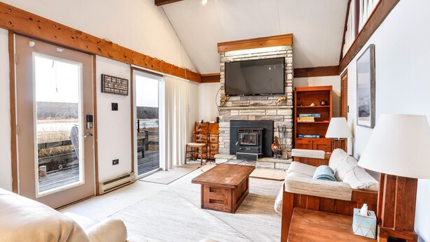 A spacious living room with a fireplace, a sofa set, a coffee table, and a television mounted above the fireplace. - Lakefront Cottage w Fireplace, Private Lake Access, Dock, Big Yard (Albrightsville)