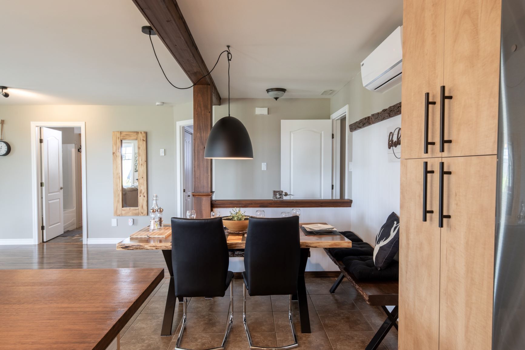 A modern kitchen with a wooden dining table, two black chairs, a pendant light, and a built-in oven.