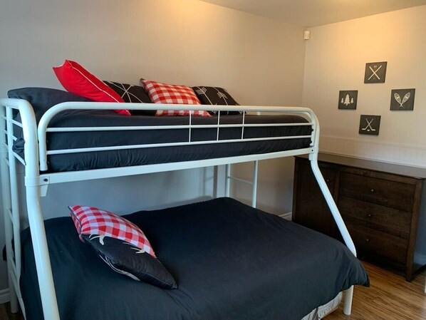 A bunk bed with black and red checkered pillows, a white metal frame, and a dark wooden dresser in the background.