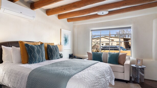 A bedroom with a large bed, a sofa, a small table, and a window with a view of a building and parked cars.