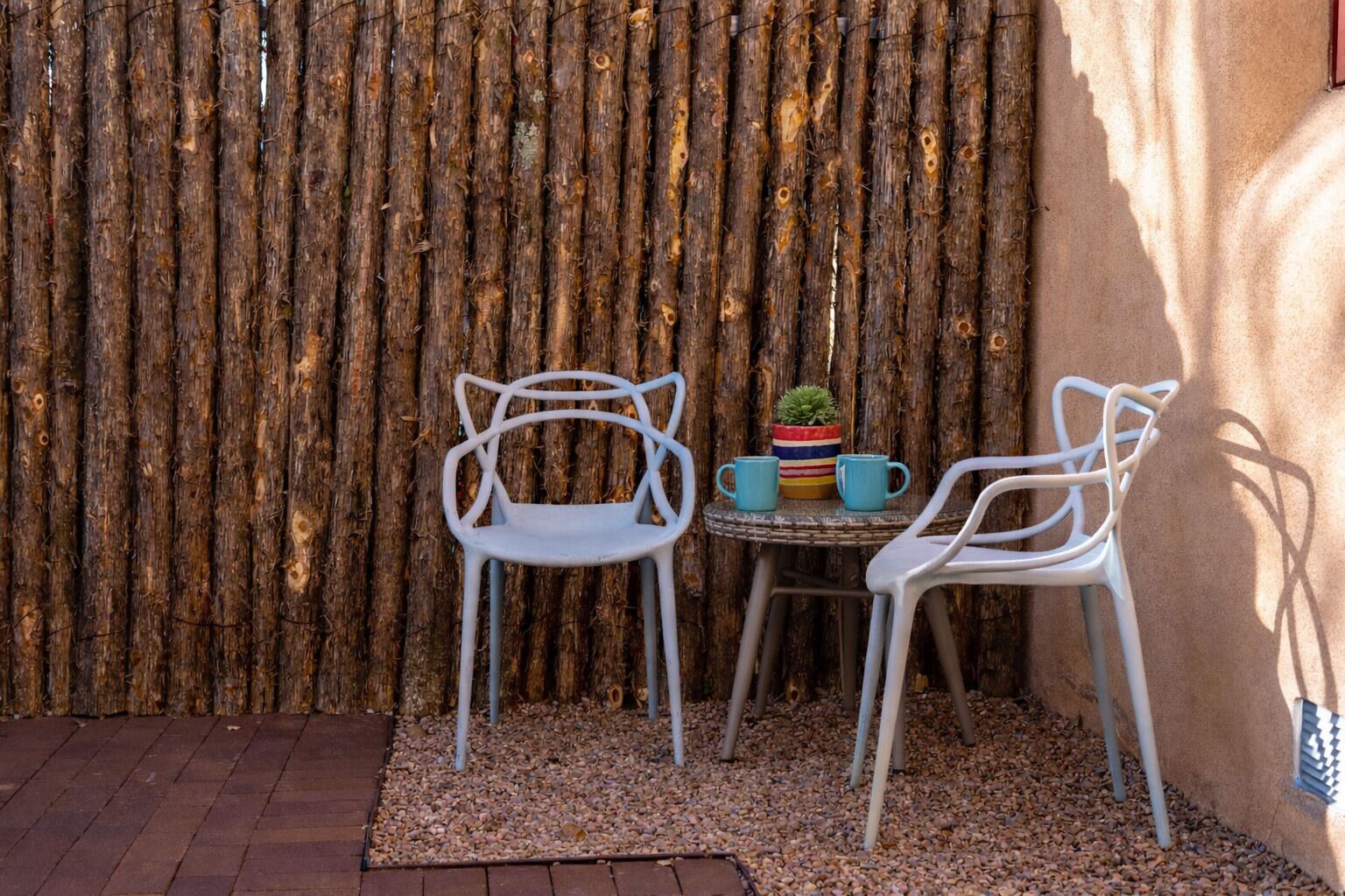 Un petit espace extérieur aménagé avec deux chaises blanches et une table ronde, le tout adossé à une clôture en bois.