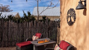 An outdoor seating area with wicker furniture, red cushions, and a fire feature.