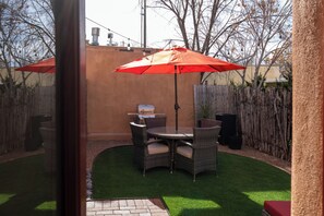 Une terrasse extérieure avec une table ronde et des chaises, un parasol rouge et un barbecue.
