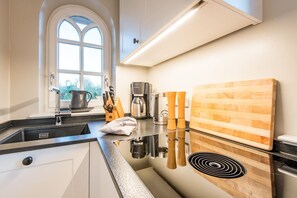 A modern kitchen with a black countertop, stainless steel appliances, a wooden cutting board, and a window with a view of greenery. - Leev Marie, Germany (Sylt)