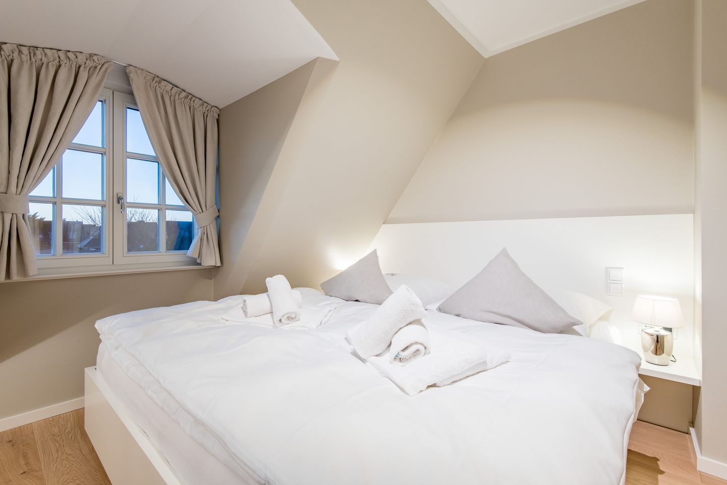 Un dormitorio con una cama grande, una mesita de noche con lámpara y una ventana con cortinas.