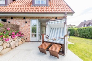 A house with a brick facade, a tiled roof, and a patio area with a striped beach chair and wooden steps. - Leev Marie, Germany (Sylt)