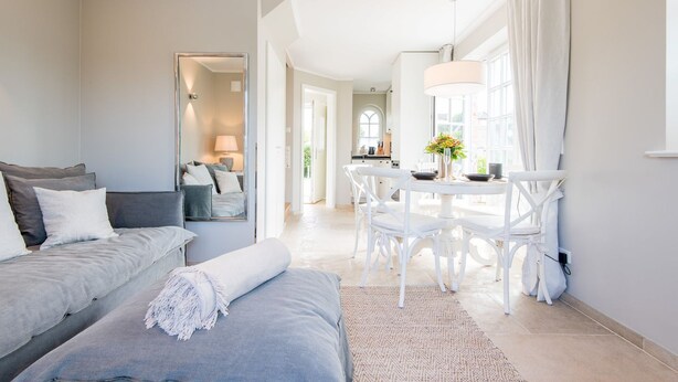 A modern, well-lit bedroom with a large bed, a sitting area, and a dining table with chairs. - Leev Marie, Germany (Sylt)