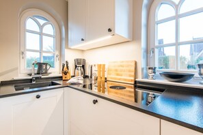 A modern kitchen with a black countertop, white cabinets, a coffee maker, and a wooden cutting board. - Leev Marie, Germany (Sylt)