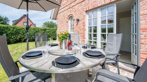 A round wooden table set for four with chairs, a large umbrella, and a bottle of Still Perle wine. - Leev Marie, Germany (Sylt)