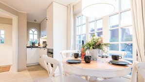A dining area with a round table, white chairs, and a vase with flowers. - Leev Marie, Germany (Sylt)