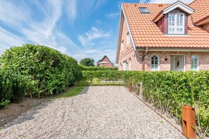 Ein Schotterweg führt zu einem Ziegelhaus mit rotem Ziegeldach und einem kleinen Fenster.