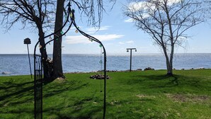 A paved walkway with a metal fence and trees, leading to a body of water.