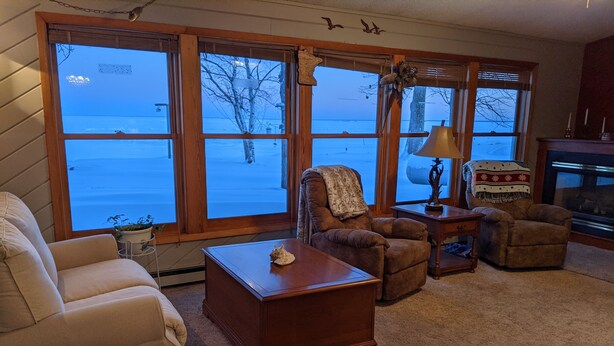 A cozy living room with a fireplace, large windows, and a view of a snowy landscape.