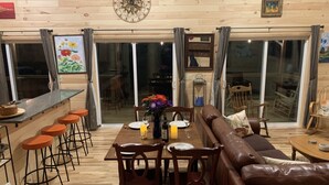 A dining area with a wooden floor, a brown leather sofa, and a bar with stools.