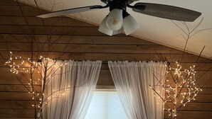 A bedroom with a bed, white curtains, a ceiling fan, and a window with curtains.