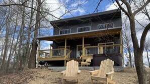 A cabin with a porch, two Adirondack chairs, and a metal barrel.