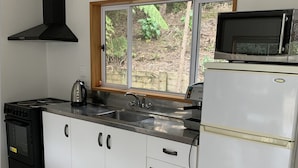 Une cuisine avec des meubles blancs, une cuisinière noire, un four à micro-ondes et une fenêtre donnant sur un paysage verdoyant.