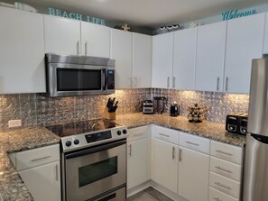 Fully equipped kitchen with stainless steel appliances, white cabinetry, and granite countertop.