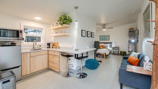 A modern kitchen with a central island, a dining area with a bar stool, a bedroom with a bed and nightstand, and a living area with a sofa and a coffee table. - #HabitueHomes - Green Spot Studio- Dog Friendly! (Boise)