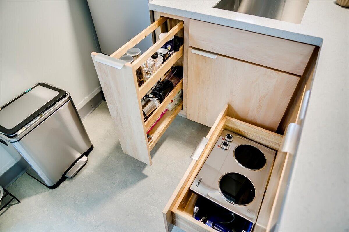 Een kleine keuken met een inbouwfornuis, een afvalbak en een houten kast met planken.