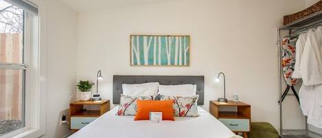 A neatly arranged bedroom with a bed, bedside tables, a wall-mounted artwork, and a window.