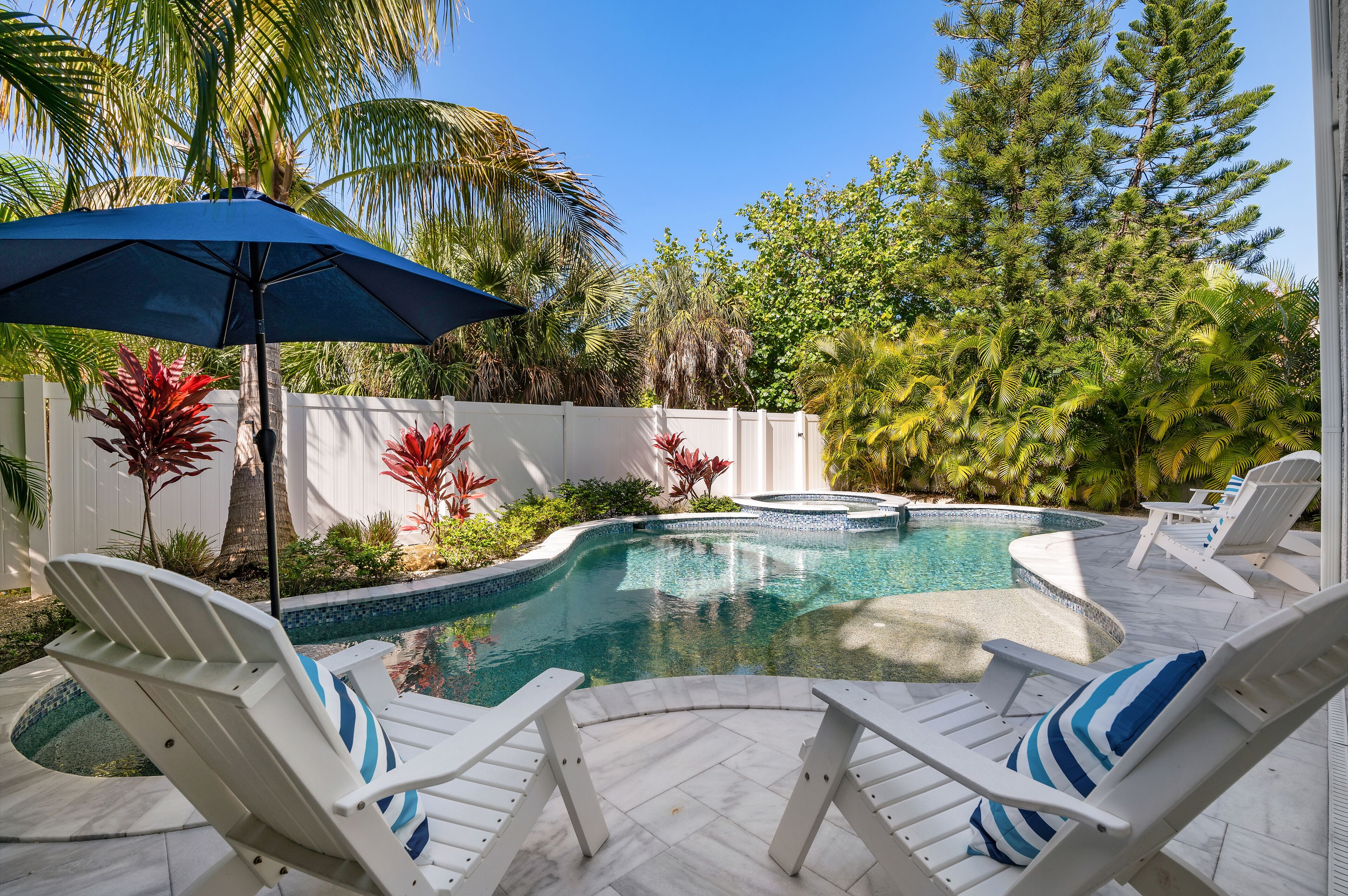Une piscine avec des chaises longues blanches et un parasol bleu.