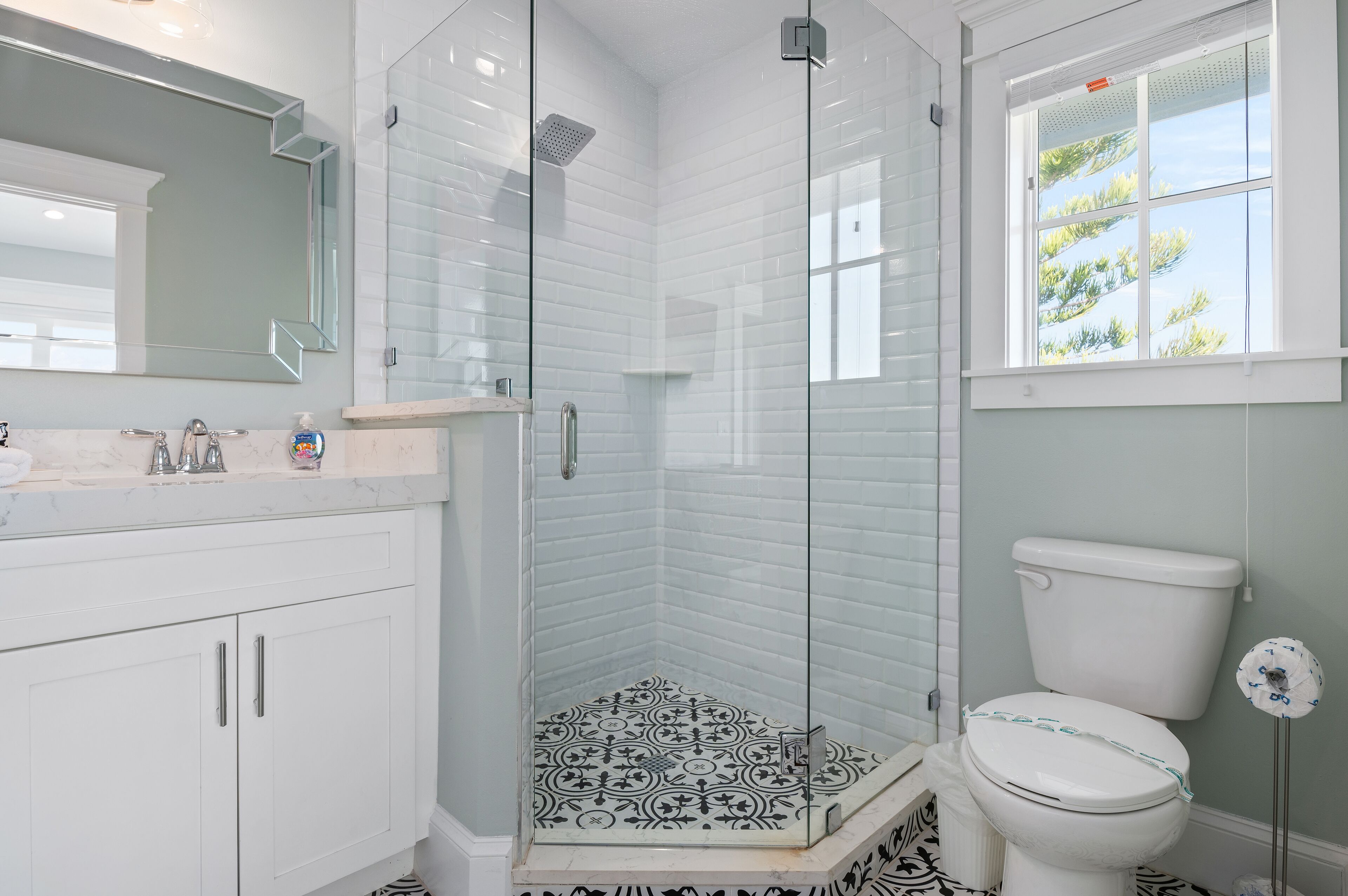 A modern bathroom with a glass-enclosed shower, a white toilet, and a large mirror above the sink.