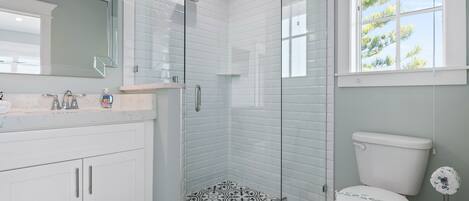 A modern bathroom with a glass-enclosed shower, a white toilet, and a large mirror above the sink.