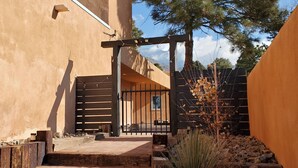 Une cour dotée d’une pergola en bois, d’un escalier menant à un portail et d’un pin.