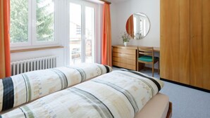 Ein Schlafzimmer mit Bett, Schreibtisch, Stuhl, Kleiderschrank und einem Fenster mit Vorhängen.