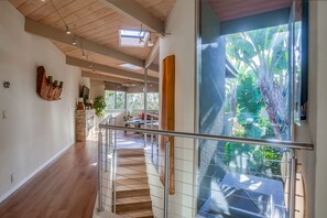 Amplo interior com escadaria de madeira, porta de vidro que dá para uma varanda e área de cozinha moderna.