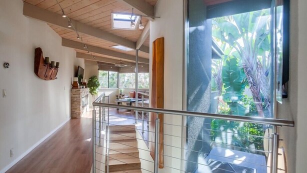 A spacious interior with a wooden staircase, a glass door leading to a balcony with plants, and a modern kitchen area. - 1.5 Blocks From The Beach: The High Tide  in Del Mar (Del Mar)