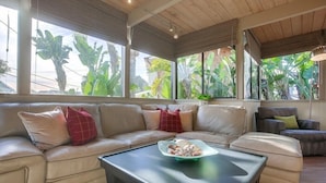 A modern living room with a beige sofa, a coffee table, and large windows with tropical plants. - 1.5 Blocks From The Beach: The High Tide  in Del Mar (Del Mar)