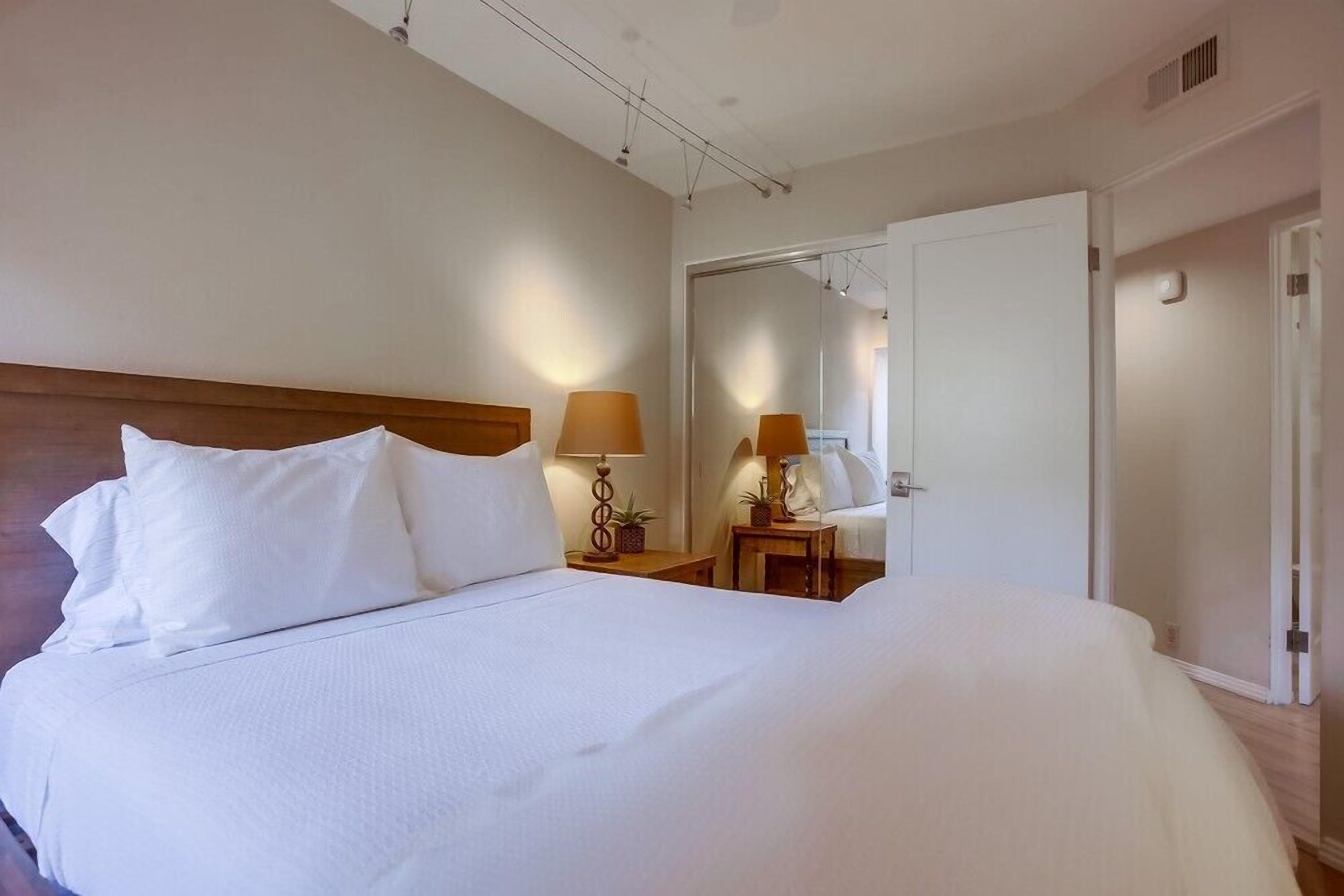 A hotel room with a large bed, two bedside tables with lamps, a mirror, and a door leading to another room.
