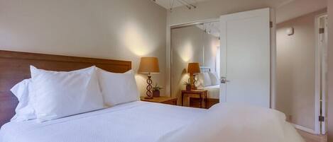 A hotel room with a large bed, two bedside tables with lamps, a mirror, and a door leading to another room.