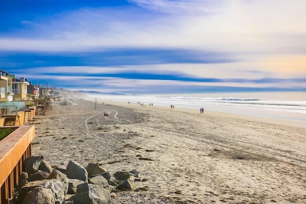 A beach with a wooden boardwalk, rocky outcrops, and a clear view of the ocean.