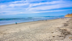A beach with a wide sandy shore, calm waves, and a clear sky.