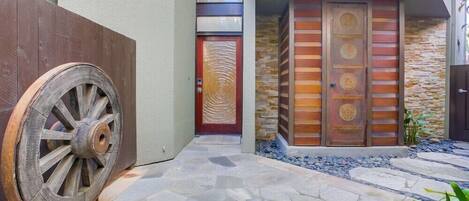 Un edificio moderno con un camino de piedra que conduce a una puerta de madera con diseño circular.