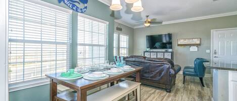 A dining area with a wooden table set for four, a brown leather couch, and a television mounted on the wall.