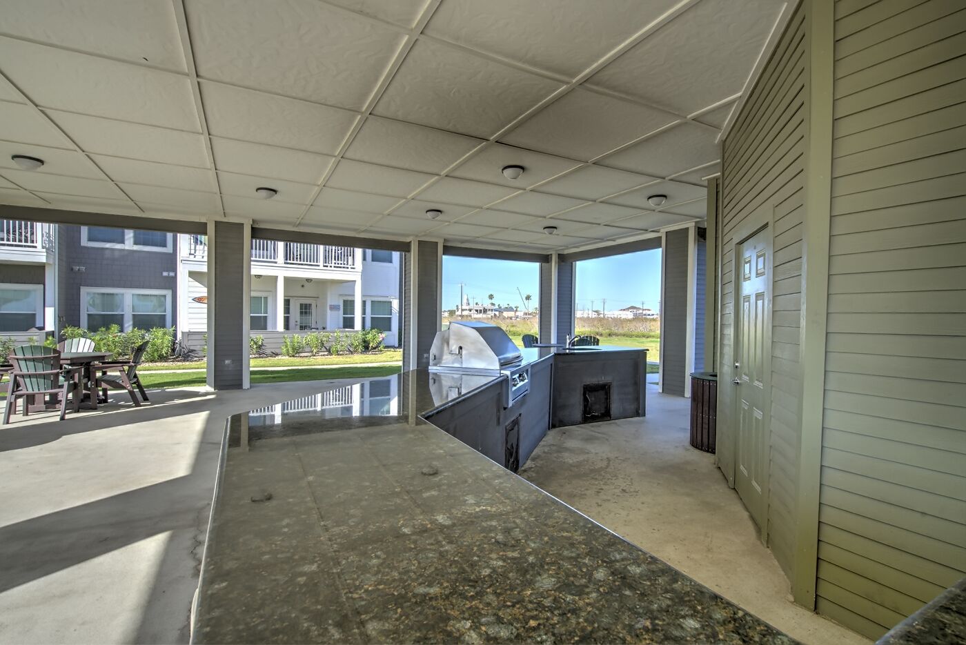 Un espace extérieur aménagé en terrasse, avec un barbecue, des sièges et une vue sur un bâtiment en arrière-plan.