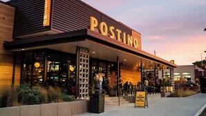 A modern building with a prominent 'POSTINO' sign, a glass storefront, and a signboard advertising $25 board and bottle. - Awesome Downtown Gilbert location | Pets welcome (Gilbert)