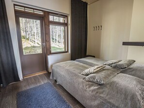 Een slaapkamer met twee bedden, een raam met uitzicht op bomen, een donker gordijn en een houten vloer.