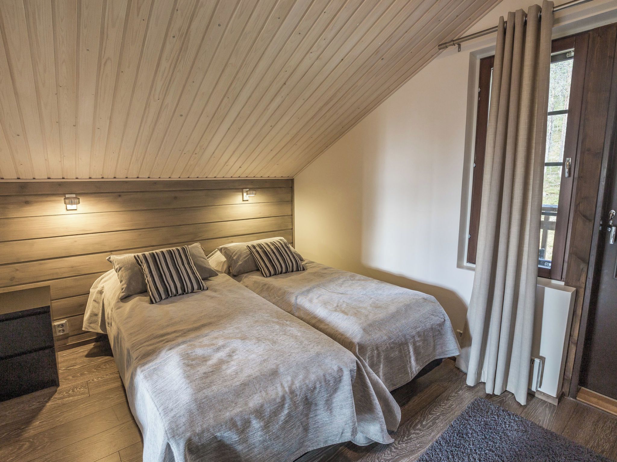 Een slaapkamer met twee bedden, een houten plafond en een deur voorzien van gordijnen.