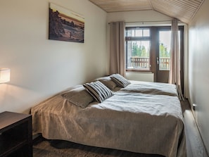 Ein Schlafzimmer mit einem Bett, einem Nachttisch, einem Bild an der Wand und einem Fenster mit Vorhängen.