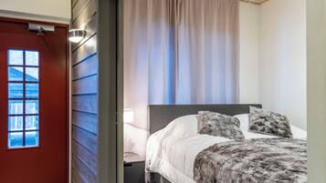 Un dormitorio con cama, mesita de noche, lámpara, ventana y puerta.
