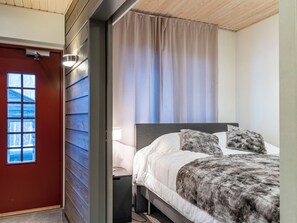 A bedroom with a bed, a nightstand, a lamp, a window, and a door.