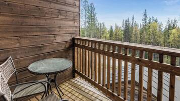 A wooden deck with a round table and two wicker chairs, overlooking a forested area.