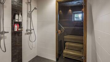 Een moderne badkamer met een douche, een glazen deur die naar een trap leidt, en toiletartikelen op een plank.