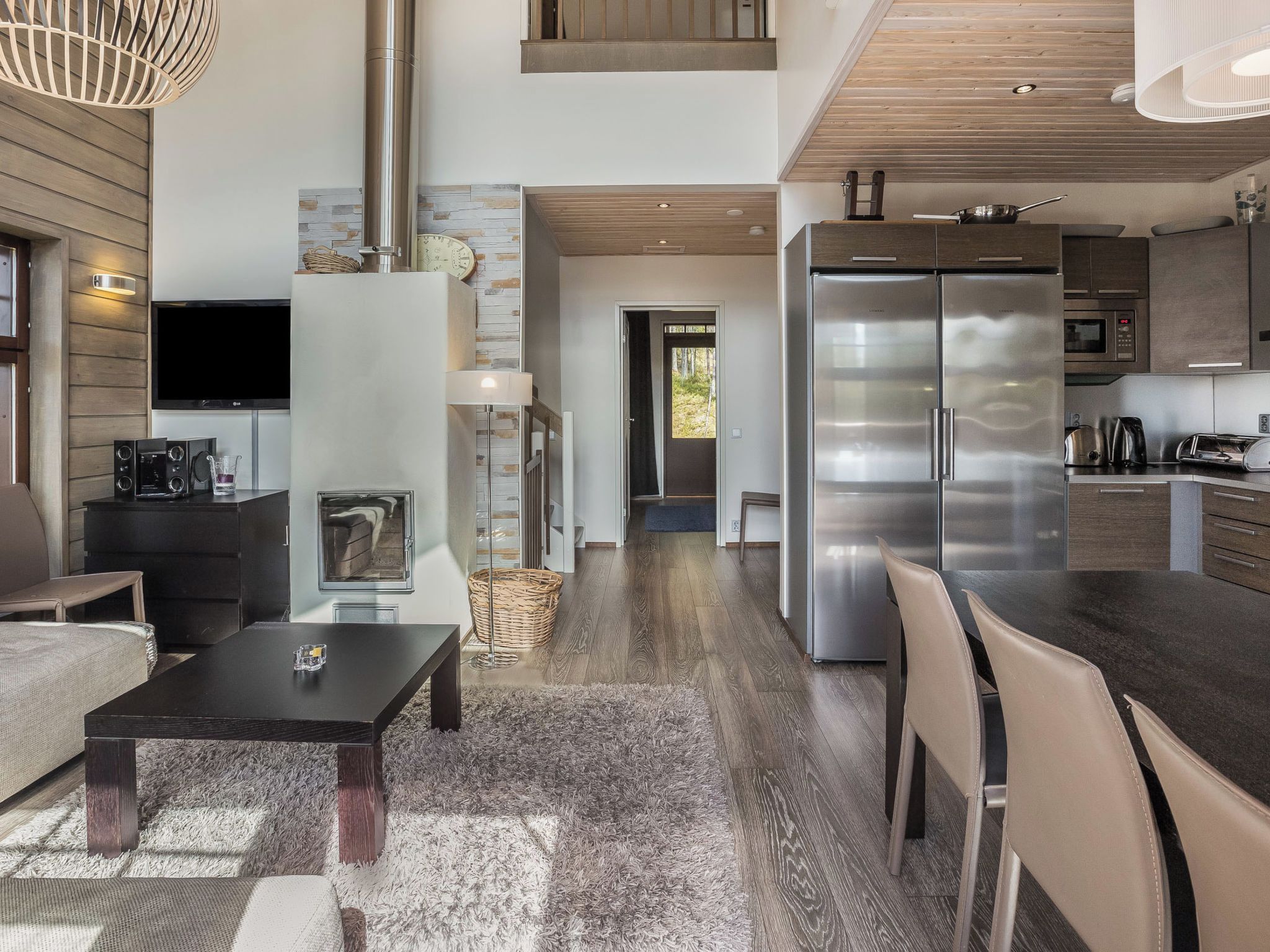 A modern kitchen with stainless steel appliances, a dining area with a table and chairs, and a living room with a sofa and a fireplace.